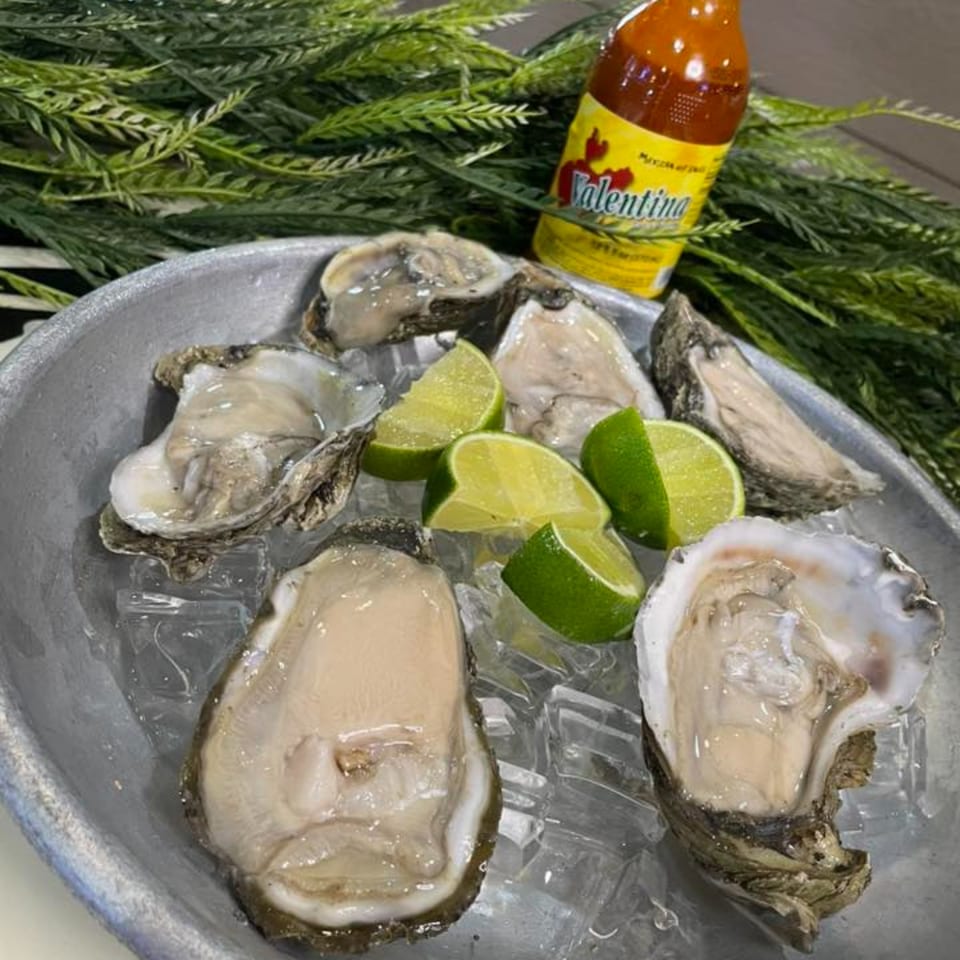 Fresh oysters on ice with lime wedges and a bottle of Valentina hot sauce.