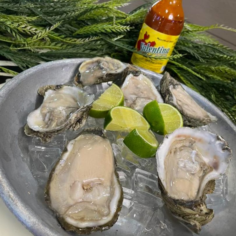 Fresh oysters on ice with lime wedges and a bottle of Valentina hot sauce.
