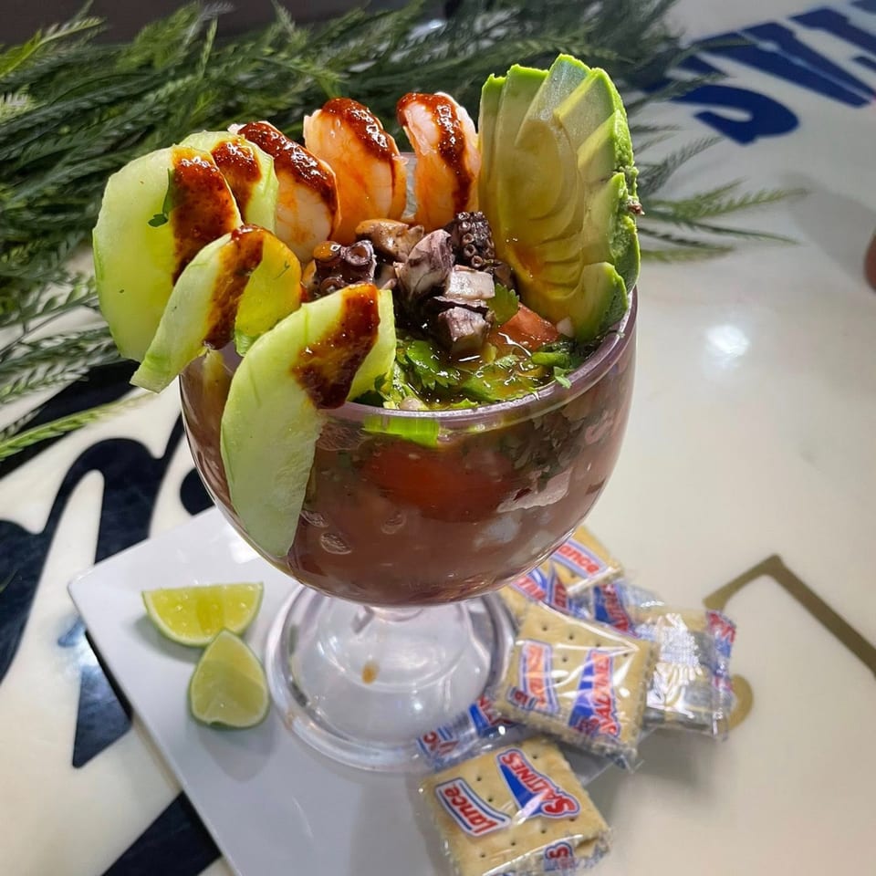 Mexican coctel de mariscos with shrimp, octopus, avocado, and cucumber in a goblet with crackers.
