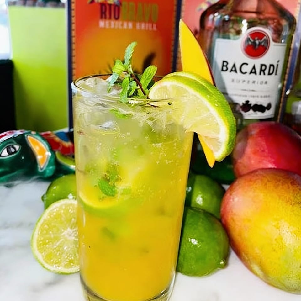 A tall glass of mango mojito with lime and mint, next to Bacardi and Rio Bravo branding.