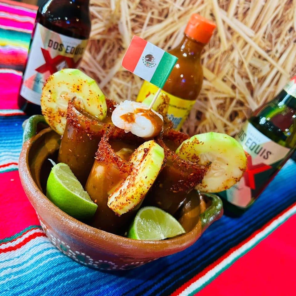 Mexican dish with shrimp, cucumber, and lime in a clay bowl, with Dos Equis bottles.