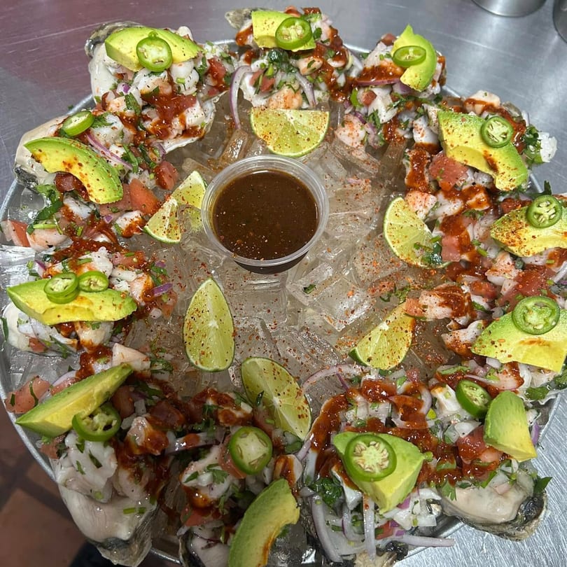 A platter of fresh oysters topped with ceviche, avocado, jalapeños, and lime, served on ice.